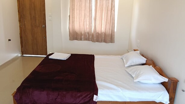 Ein Einzelbett mit Holzrahmen, weißer Bettwäsche und einer dunkelroten Decke.