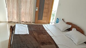 Ein Bett mit brauner Decke und weißen Bettwäsche, eine Holztür und ein Fenster mit Vorhängen.