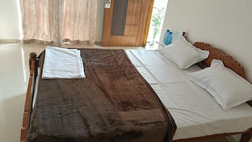 Una cama con cubierta marrón y ropa de cama blanca, una puerta de madera y una ventana con cortinas.