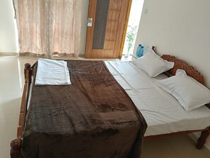 Una cama con cubierta marrón y ropa de cama blanca, una puerta de madera y una ventana con cortinas.