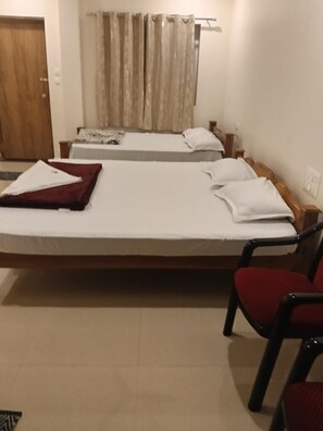 Una habitación de hotel con dos camas, un armario de madera, una silla roja y una cortina.