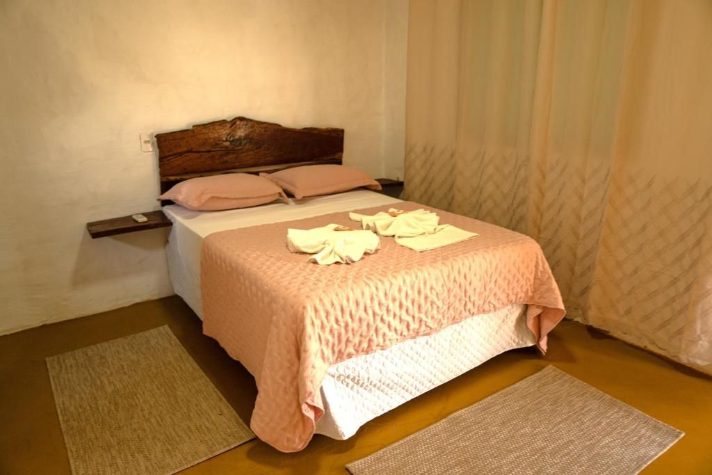 Una cama individual con cabecera de madera, una colcha rosa y dos almohadas. Hay dos alfombras en el suelo.