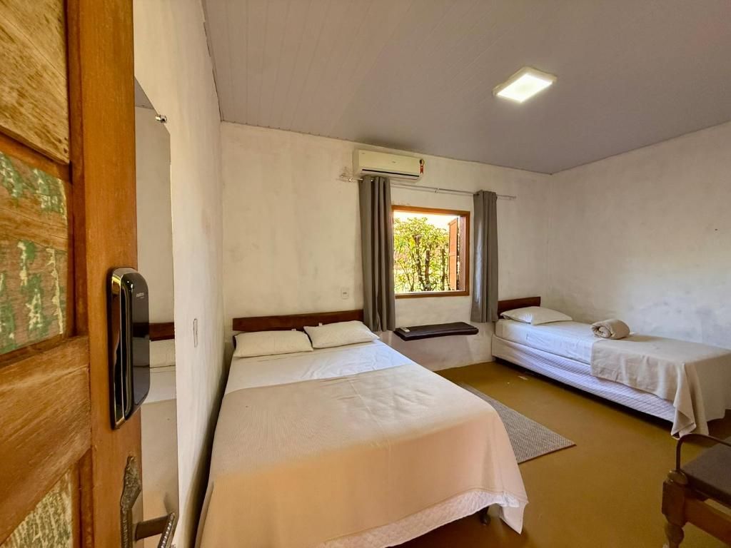 Una habitación con dos camas, una ventana con cortinas, un equipo de aire acondicionado y una puerta de madera.