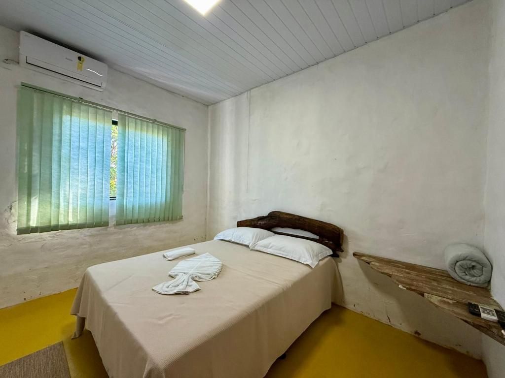 A single bed with a wooden headboard, a bedside table with a rolled-up towel, and a window with green curtains.