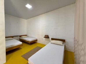 Una habitación con tres camas individuales, un estante pequeño y suelo amarillo.