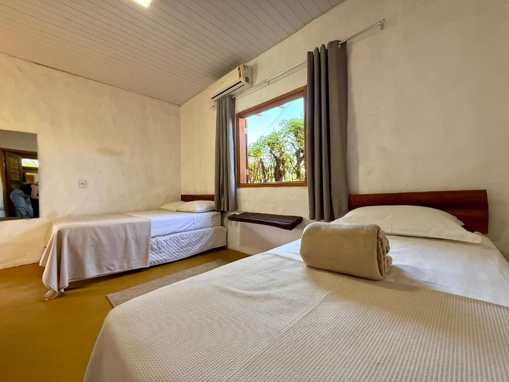 A hotel room with two beds, a window with curtains, and an air conditioning unit on the wall.