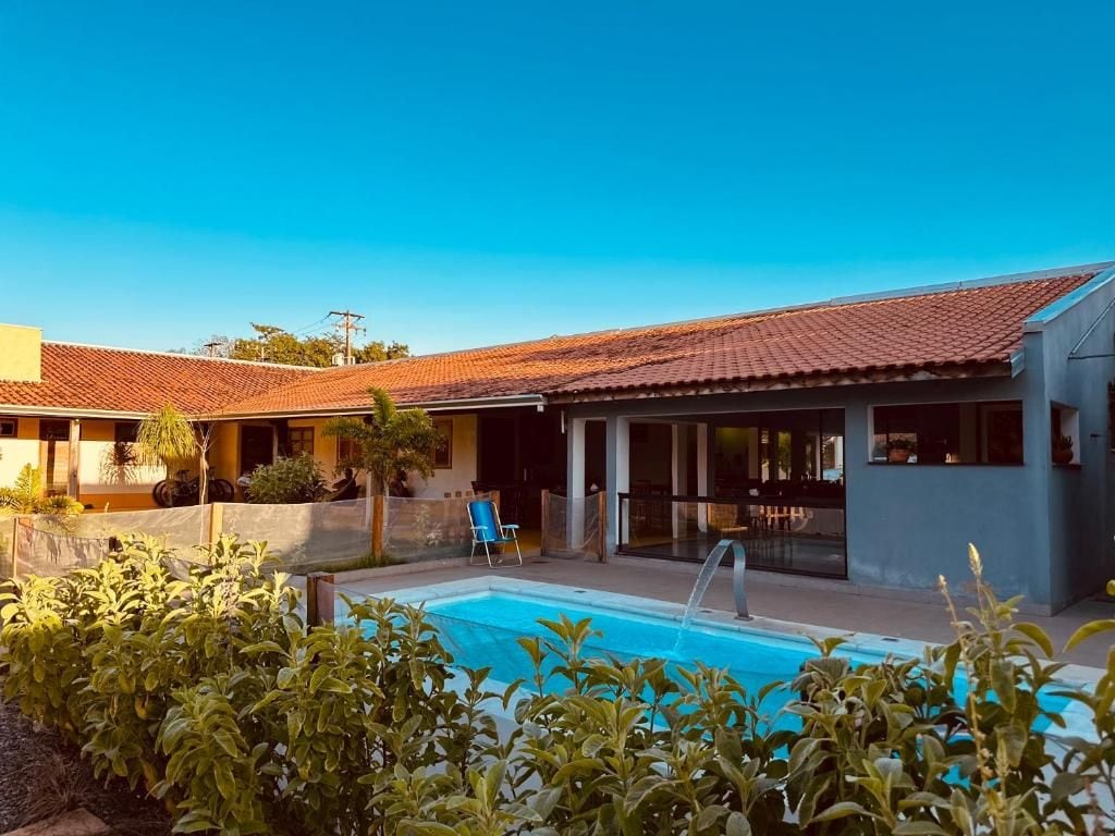 A pool area with a clear blue sky, a covered patio, and a building with a tiled roof.