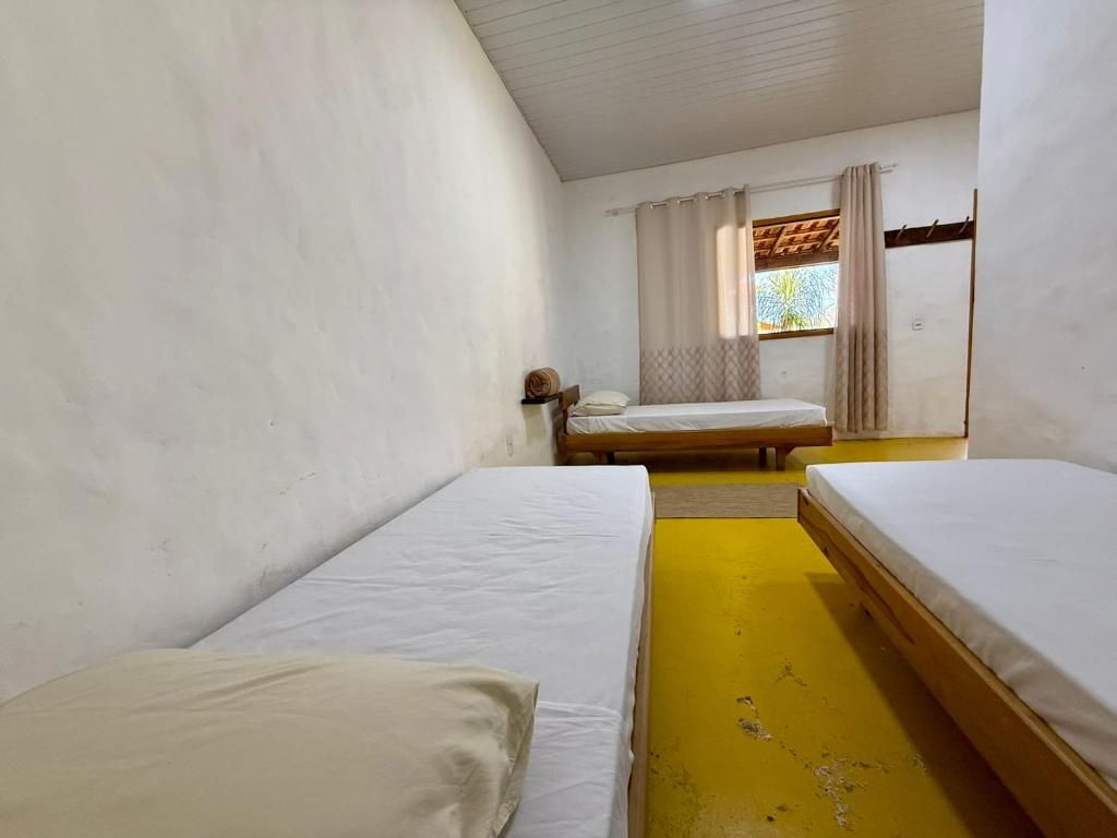 A room with two single beds, a window with curtains, and a wooden ceiling.