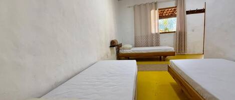 A room with two single beds, a window with curtains, and a wooden ceiling.