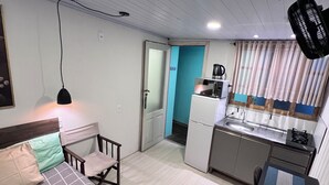 Quarto de hotel compacto com cama, escrivaninha, cozinha compacta e banheiro.
