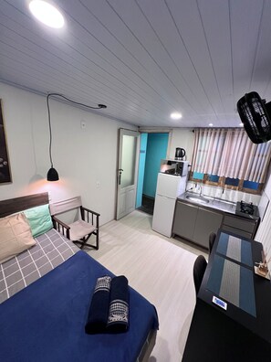 Habitació d'hotel senzilla amb llit, escriptori, zona de cuina i bany.