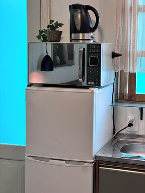 Cuina compacta amb un frigorífic blanc, un microones negre i un bullidor a la part superior.