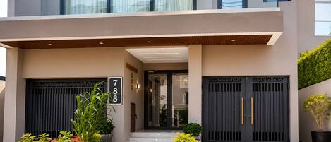 A modern two-story building with a balcony, large doors, and potted plants.
