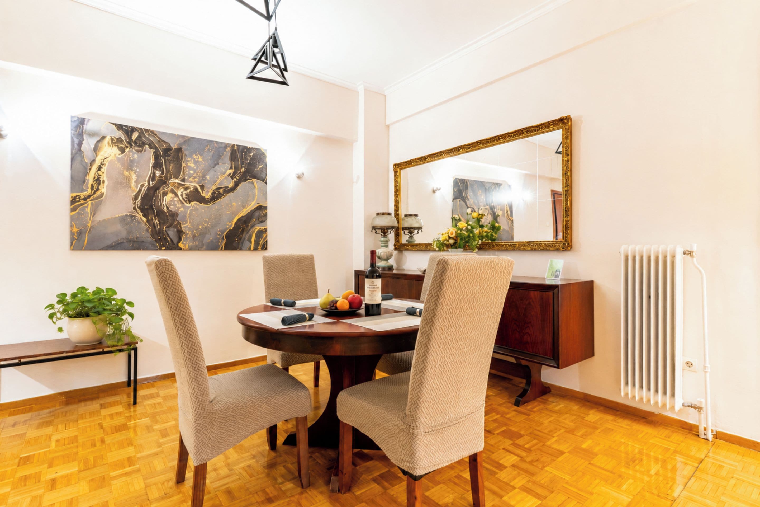 Un'area pranzo con un tavolo rotondo, quattro sedie, un grande quadro astratto, uno specchio e un termosifone.