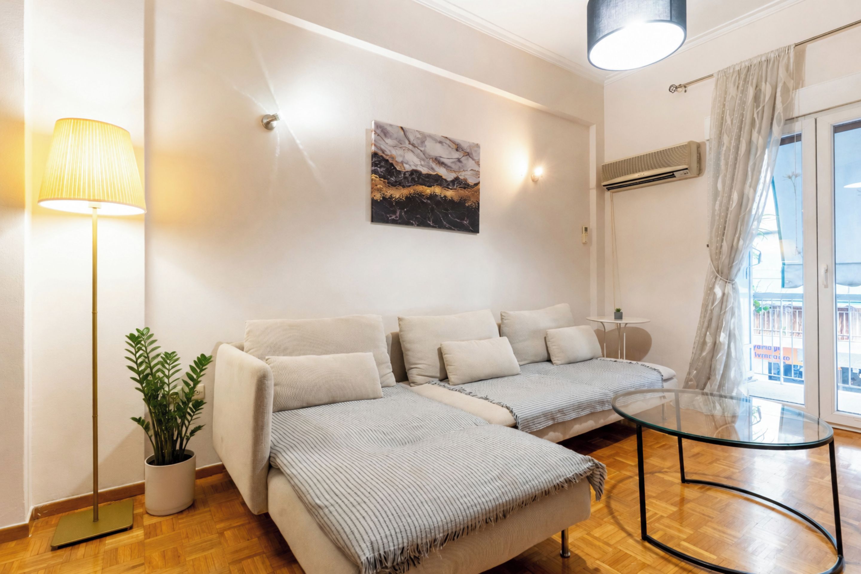 Un salon moderne avec un canapé, une table basse en verre, une lampe et un tableau accroché au mur.