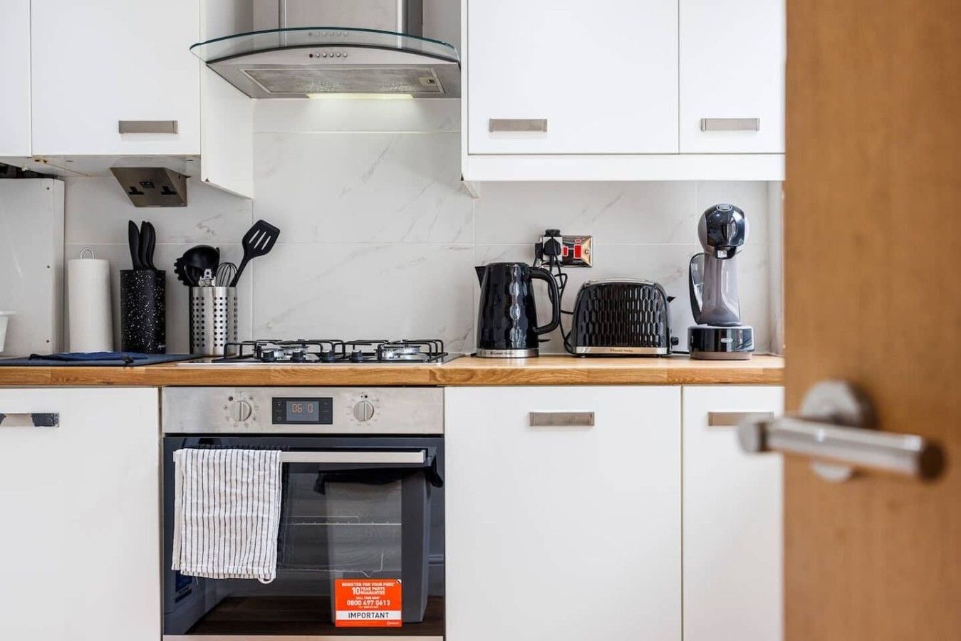 Eine moderne Küche mit weißen Schränken, einer Edelstahl-Dunstabzugshaube, einem Toaster, einem Wasserkocher und einer Kaffeemaschine.