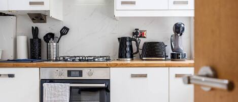A modern kitchen with white cabinets, a stainless steel range hood, a toaster, a kettle, and a coffee maker.