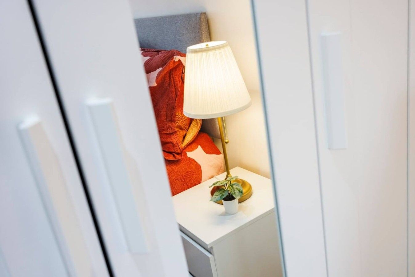 Ein Schlafzimmer mit einem Bett, einer Nachttischlampe und einem kleinen Topfpflanzen.