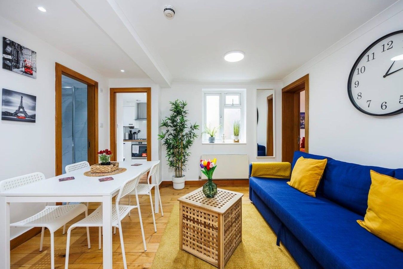 Una sala de estar moderna con un sofá azul, una mesa de comedor blanca y un reloj de pared grande.