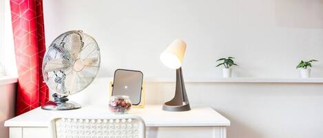 A white desk with a standing fan, a lamp, and a small potted plant.