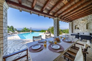 Un área de comedor al aire libre con piscina y vista al mar.