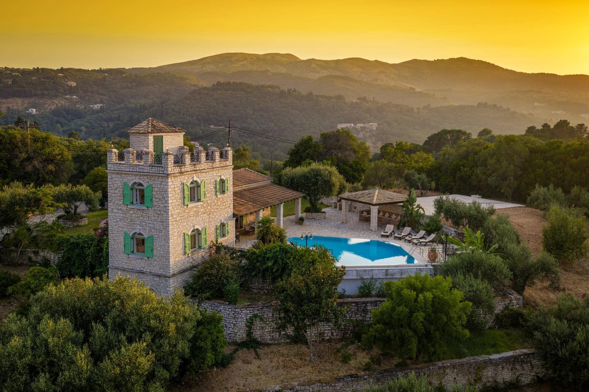 A stone tower with a swimming pool and lounge chairs in a mountainous area.