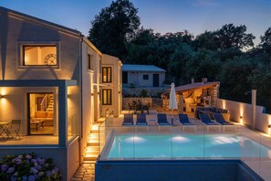 Ein modernes Haus mit Swimmingpool, Sitzgelegenheiten im Freien und einem Steinofen.
