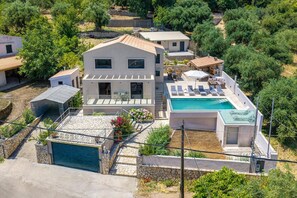 Ein modernes, zweistöckiges Haus mit Swimmingpool, überdachter Terrasse und Garage.