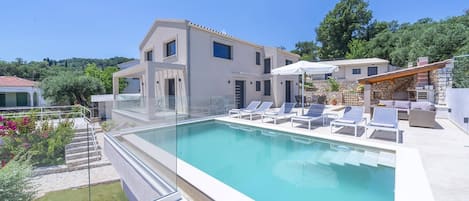 Un espace piscine moderne avec des chaises longues et un bâtiment en pierre en arrière-plan.
