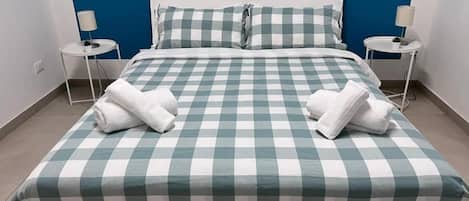 Un lit avec une couvre-lit à carreaux, deux oreillers blancs et deux serviettes blanches pliées sur le lit.