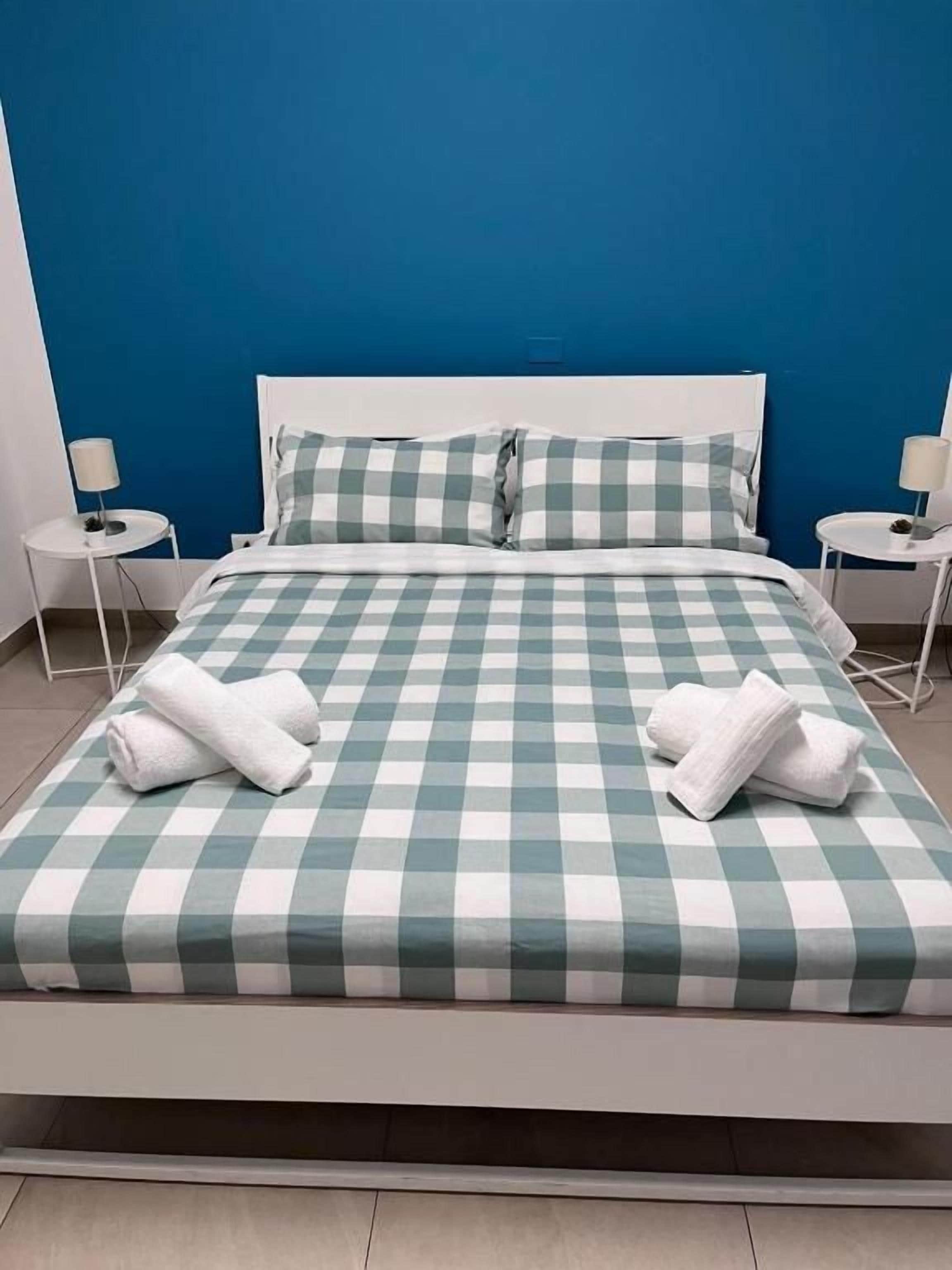 Ein Bett mit karierter Bettdecke, zwei Kissen und zwei aufgerollte Handtücher.