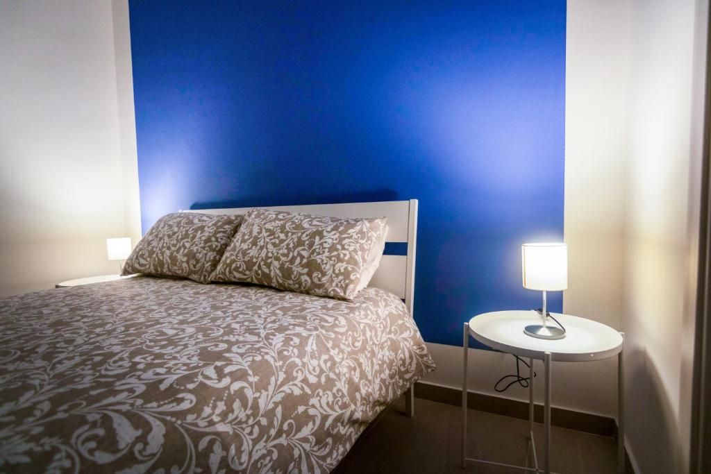 Un dormitorio con una cama, una mesita de noche con una lámpara y una pared azul.