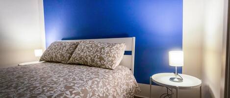 A bedroom with a bed, a bedside table with a lamp, and a blue wall.