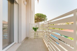 A balcony with a white railing, a potted plant, and a view of a tree and buildings. - Cilea Apartment near Venice (Noale)