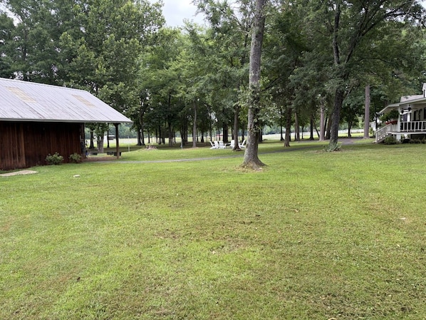 A grassy area with a wooden structure and a building with a porch. - Just West of Little Rock Retreat (Paron)