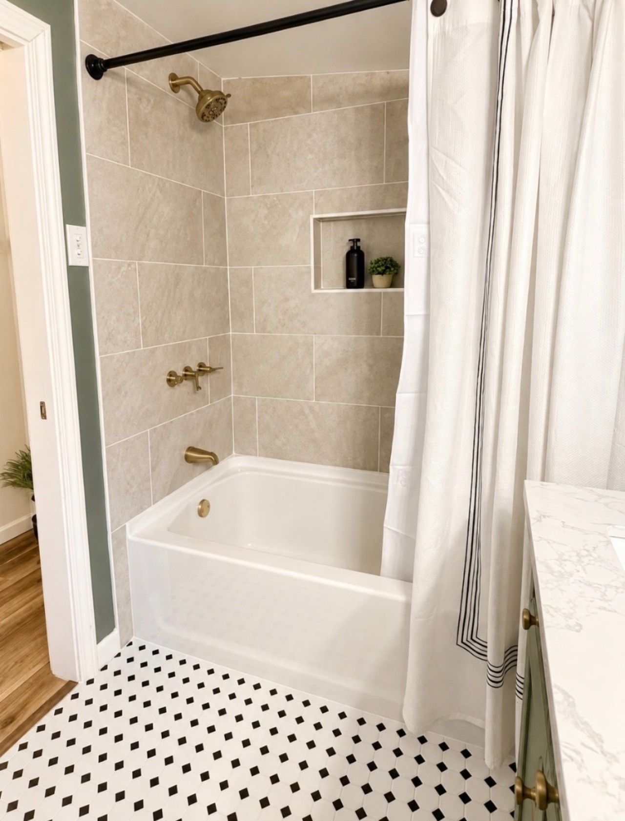 A bathroom with a bathtub, a shower, and a toilet. There is a shelf with toiletries and a potted plant. The floor has a black and white patterned tile.