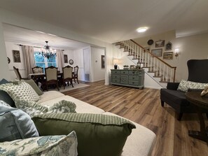 A living room with a sofa, a dining area with chairs, a staircase, and a side table with a lamp.