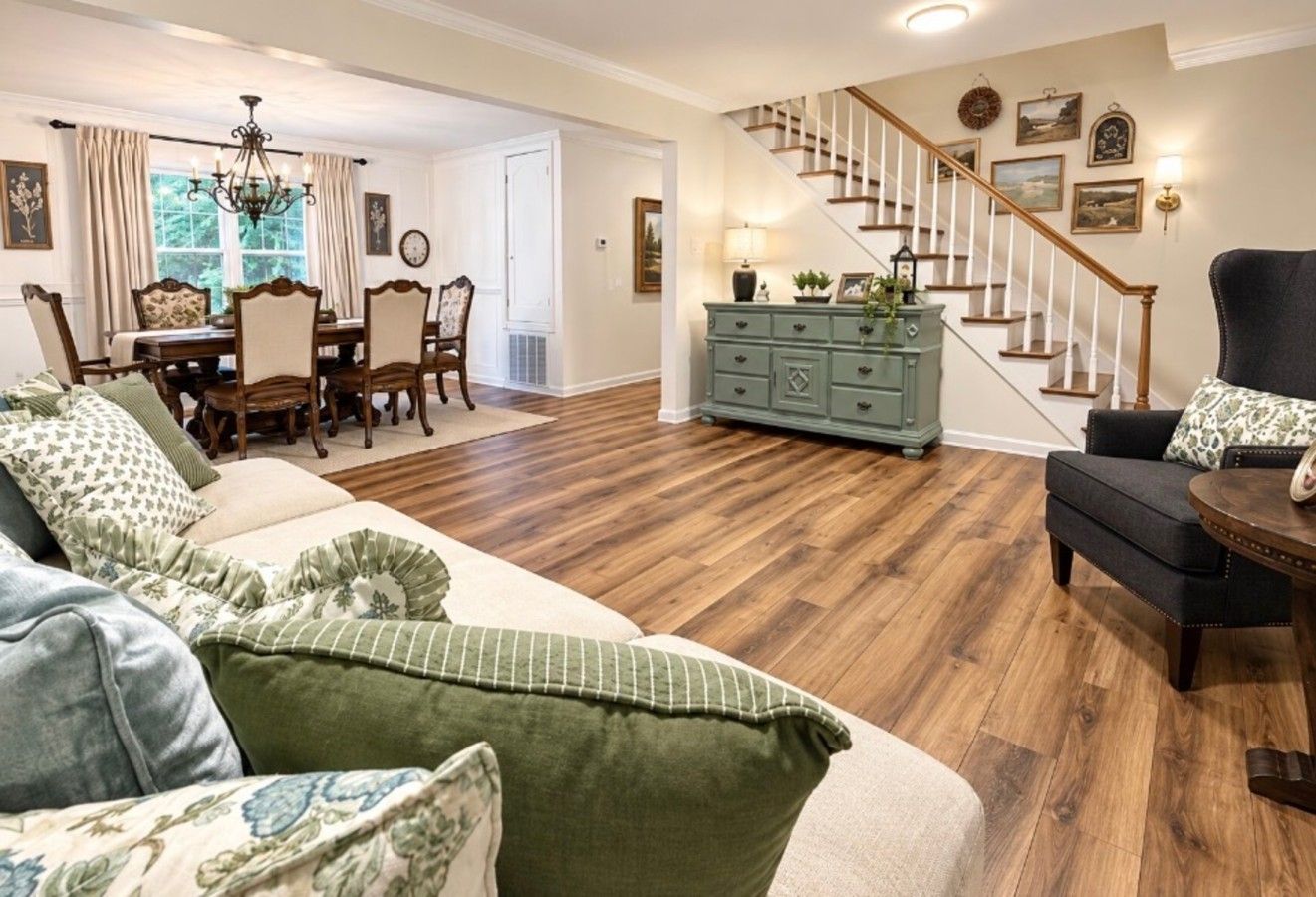A living room with a sofa, a dining area with a table and chairs, a staircase, and a green dresser.