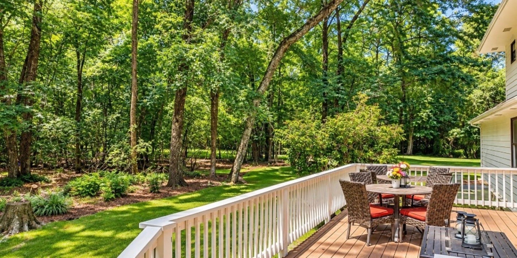 A deck with outdoor furniture, surrounded by a white fence, set in a wooded area.