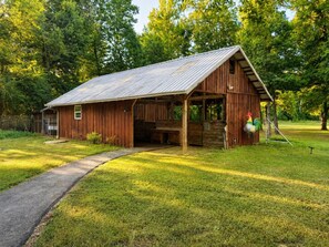 A rustic wooden barn with a metal roof, a covered porch, and a gravel path leading to it. - Barn Apartment | Peaceful Views | Just West of Little Rock (Paron)