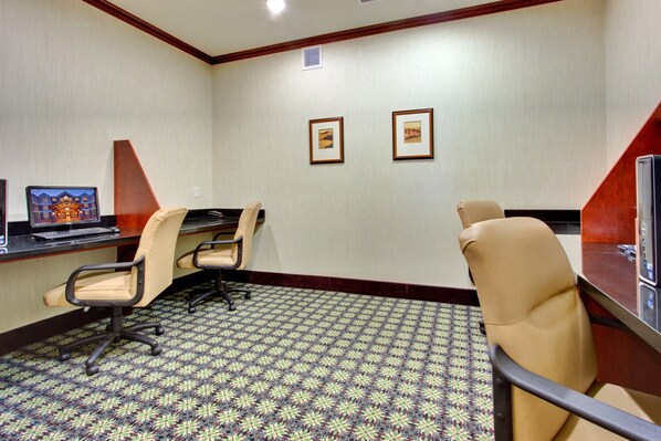 A conference room with a patterned carpet, two framed pictures on the wall, and a desk with a computer and chair.