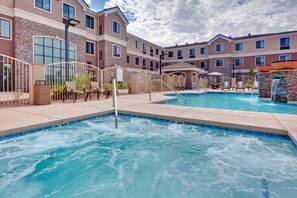 A swimming pool area with lounge chairs and a stone waterfall feature.