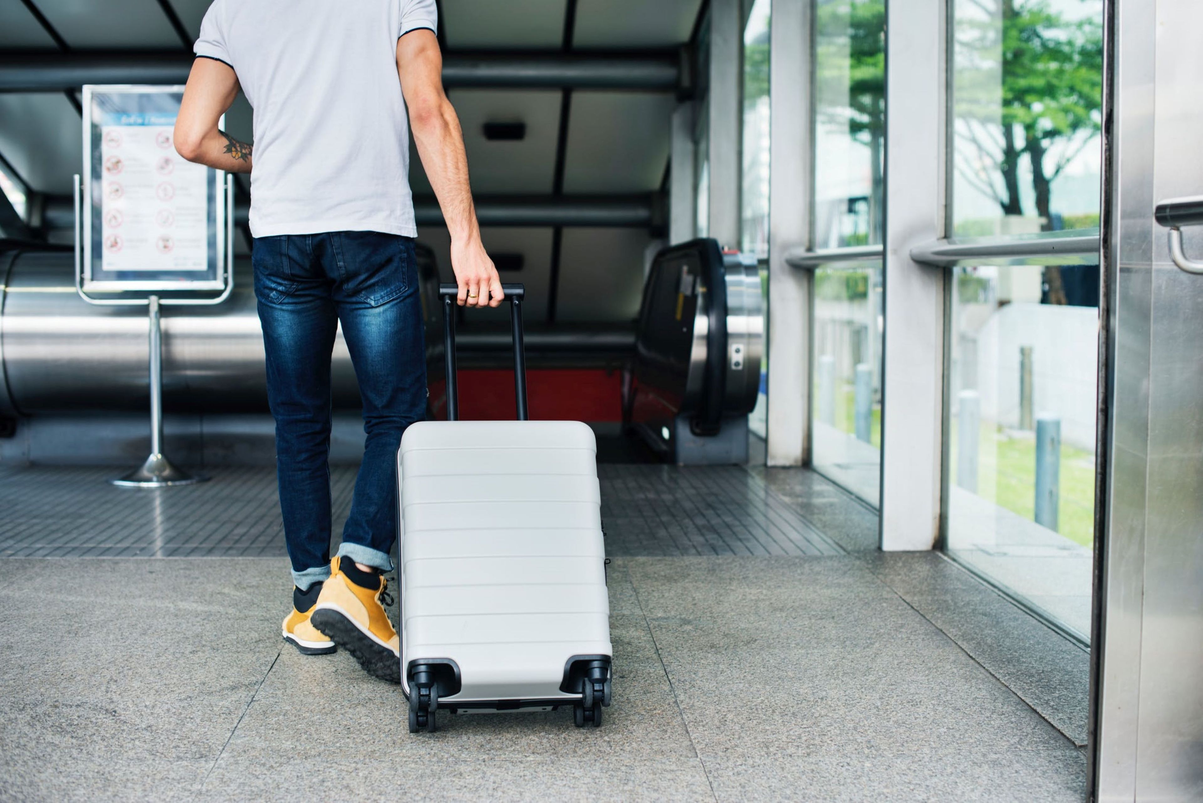 A person with a suitcase in an indoor setting with a metallic floor, a glass wall, and a metal railing.