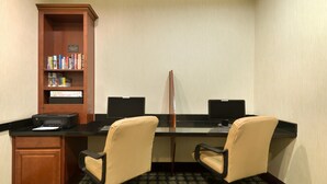 Sala de conferência com duas mesas, cadeiras, uma estante e uma impressora.