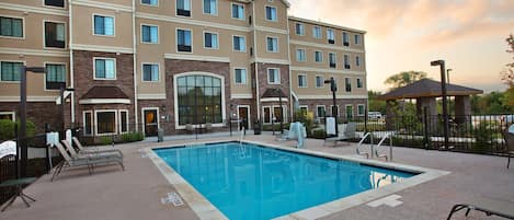 A hotel with a swimming pool, lounge chairs, and a covered seating area.