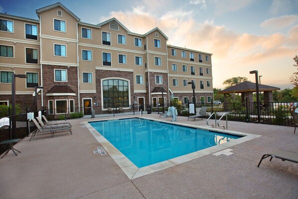 A hotel with a swimming pool, lounge chairs, and a covered seating area.