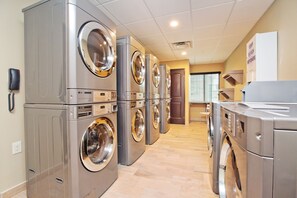 A laundry facility with multiple LG washing machines and dryers, a phone on the wall, and a sign indicating soap and detergent dispensers.