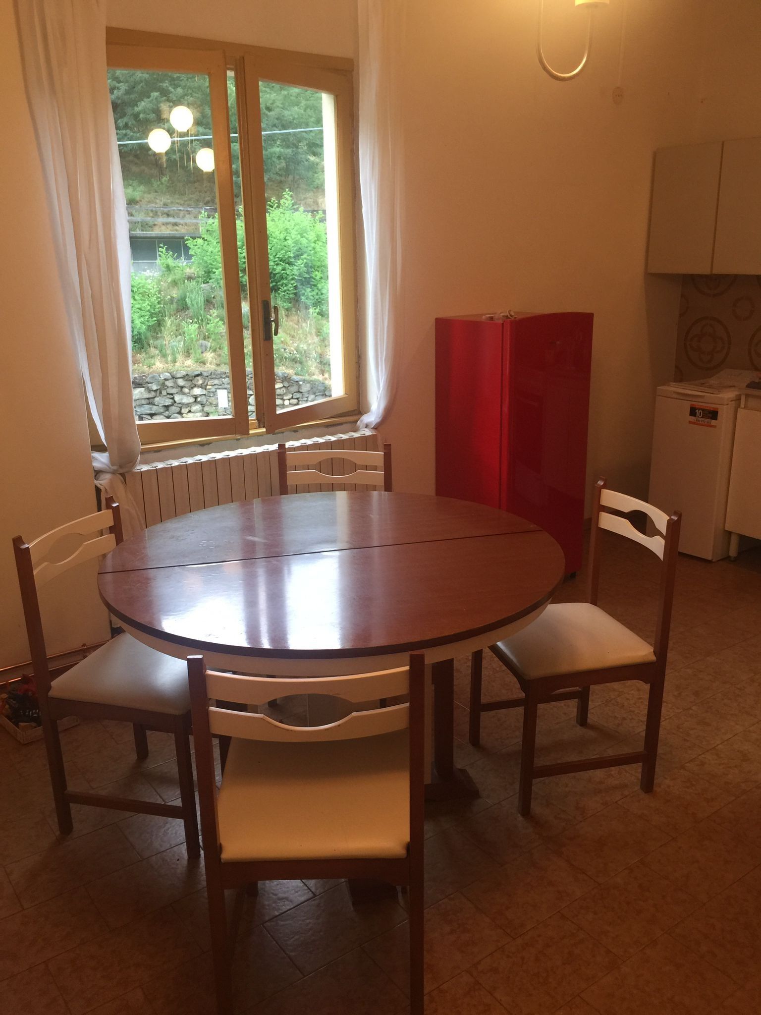 Ein Essbereich mit einem runden Tisch, vier Stühlen, einem Fenster mit Vorhängen, einem roten Schrank und einem Kühlschrank.