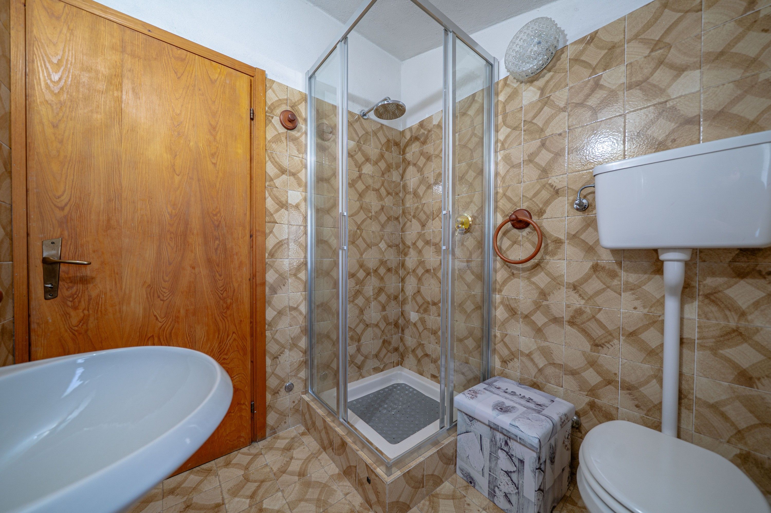 Ein Badezimmer mit Holztür, Duschkabine aus Glas, einer weißen Badewanne und Toilette.