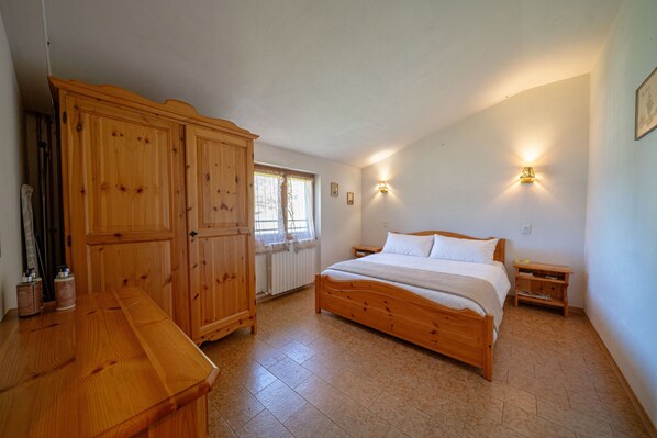 A bedroom with a wooden bed, a wooden wardrobe, a small bedside table, and a window with curtains.